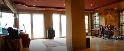 Spacious, bright live room with tall windows, a rug and the drum kit beyond
