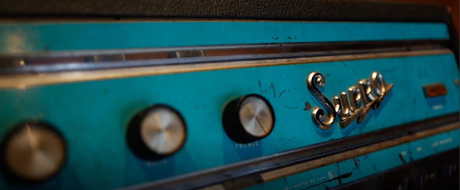 Teal front panel of a vintage Supro amplifier with chrome knobs