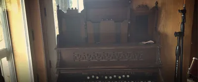 Antique carved wooden pump organ beside a window and a mic stand