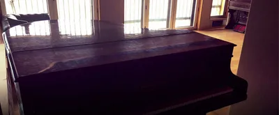 Closed grand piano silhouetted against the live room's tall windows
