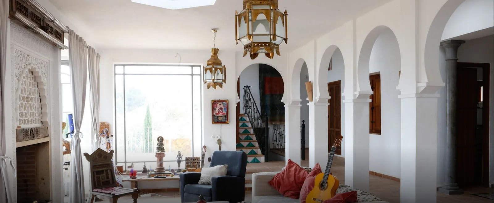 White living room with horseshoe arches, Moorish lanterns and a guitar on the sofa