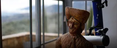 Carved wooden figure in a turban beside a telescope and a window over the valley
