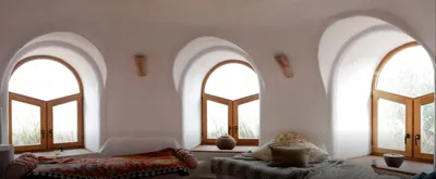 White vaulted bedroom with arched wooden windows and low beds draped in throws
