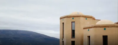 Ochre domed towers with turquoise tiles, cloud-topped mountains behind