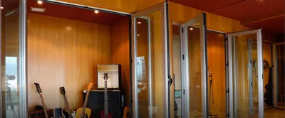 Guitars and an amp inside a wood-lined booth with folding glass doors