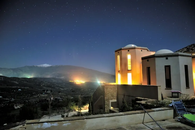 Domed towers lit at night under a starry sky, snow-capped Sierra Nevada beyond